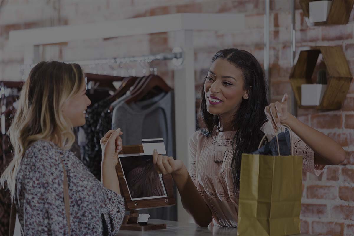 A mixed race African American woman working in a clothing store at the checkout counter, helping a customer.  The cashier is handing the customer her credit card and a shopping bag.